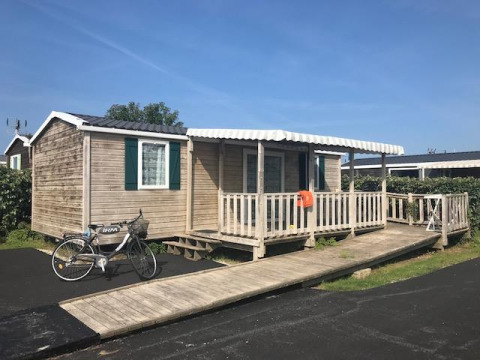 Casa mobile chiamata Mobile home Comfort PMR HELIOS con rampa, veranda e bicicletta sotto il cielo azzurro.