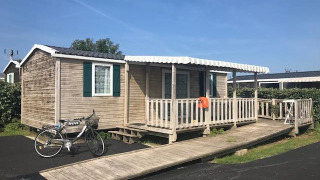 Casa móvil llamada Mobile home Comfort PMR HELIOS con rampa, porche y bicicleta bajo el cielo azul.