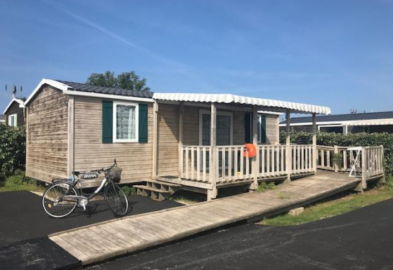 Mobile home named Mobile home Comfort PMR HELIOS with ramp, veranda, bicycle, and clear blue sky.