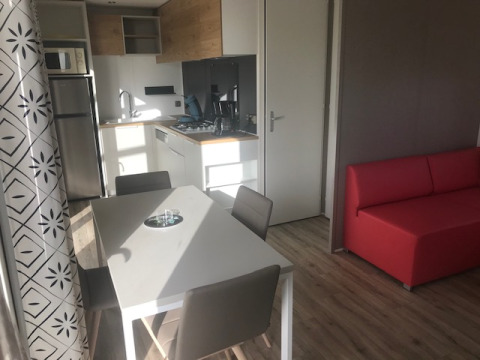 Cucina e zona pranzo di casa mobile moderna con divano rosso e arredo in legno chiaro al Flower Camping La Pointe du Talud.