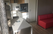 Cucina e zona pranzo di casa mobile moderna con divano rosso e arredo in legno chiaro al Flower Camping La Pointe du Talud.