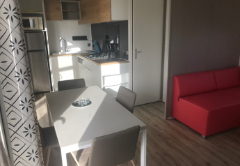 Cucina e zona pranzo di casa mobile moderna con divano rosso e arredo in legno chiaro al Flower Camping La Pointe du Talud.