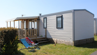 Vista esterna della Mobile home Premium HORIZON con veranda coperta e sdraio sul prato al sole.