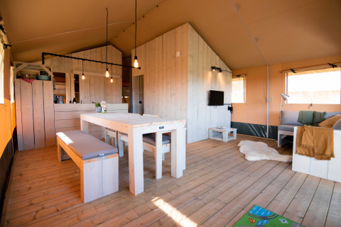 Binnenaanzicht van De Lodge met houten meubels, eettafel, zithoek en veel natuurlijk licht.