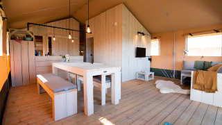 Indvendig udsigt af De Lodge med træmøbler, spisebord, sofaområde og lyse farver i rummelig atmosfære.