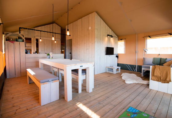 Binnenaanzicht van De Lodge met houten meubels, eettafel, zithoek en veel natuurlijk licht.