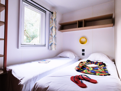 Helles Zimmer im Mobile Home Premium auf dem Campingplatz La Vallée Heureuse mit zwei Einzelbetten und Fenster.