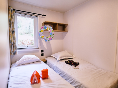 Slaapkamer in Mobile Home Premium op Camping La Vallée Heureuse in Frankrijk met twee enkele bedden.