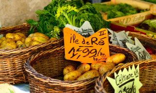 Fresh fruit and vegetables displayed in wicker baskets at a market, with handwritten signs and bright colors.