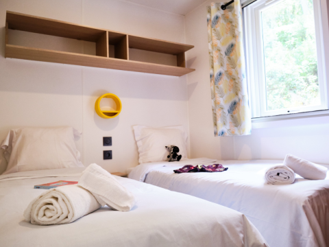 Twee eenpersoonsbedden met witte lakens in een mobilhome op Camping La Vallée Heureuse in Frankrijk, raam.