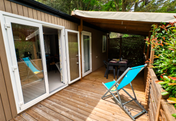 Buitenterras aan Mobile home Premium Large met houten vlonder, blauwe ligstoel en eettafel onder afdak.