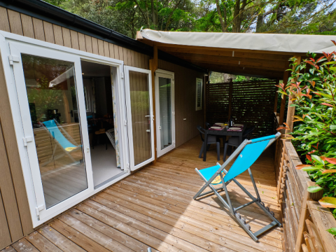 Terrasse extérieure au Mobile home Premium Large avec plancher en bois, chaise longue bleue et coin repas couvert.