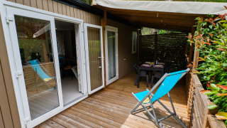 Buitenterras aan Mobile home Premium Large met houten vlonder, blauwe ligstoel en eettafel onder afdak.