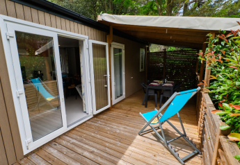 Terrasse eines Mobile home Premium Large mit Holzdeck, Liegestuhl und überdachtem Essbereich.
