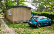 Auto blu vicino alla casa mobile «Premium Large» al campeggio La Vallée Heureuse, Francia, circondata dal verde.