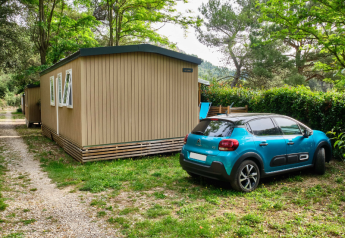 Blaues Auto neben Mobilheim 'Premium Large' auf Campingplatz La Vallée Heureuse in Frankreich, grüne Umgebung.