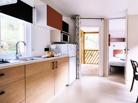 Cuisine de mobil-home moderne avec meubles en bois, vue sur chambre et terrasse à La Vallée Heureuse.