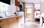Cocina de casa móvil moderna con armarios de madera y vista al dormitorio y terraza en La Vallée Heureuse.