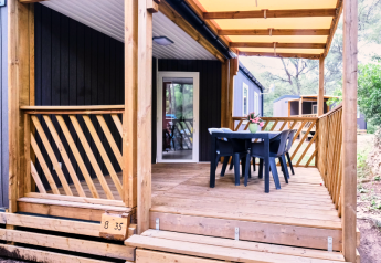 Overdekt terras van Mobile Home Premium met houten railing, tafel, vier stoelen en uitzicht op bos.