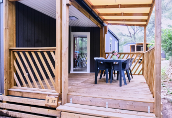 Überdachte Terrasse des Mobile Home Premium mit Holzgitter, Tisch, vier Stühlen und Waldblick.