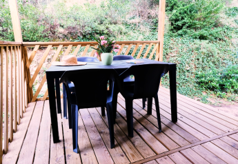 Terrasse mit Holzboden, schwarzen Stühlen und Tisch, Blumen und Hut im Mobile Home Premium in Frankreich.