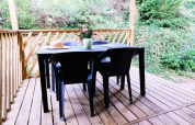 Terraza de madera con mesa y sillas negras, jarrón de flores y sombrero en Mobile Home Premium, Francia.