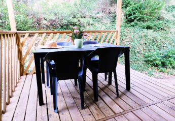 Terrasse mit Holzboden, schwarzen Stühlen und Tisch, Blumen und Hut im Mobile Home Premium in Frankreich.