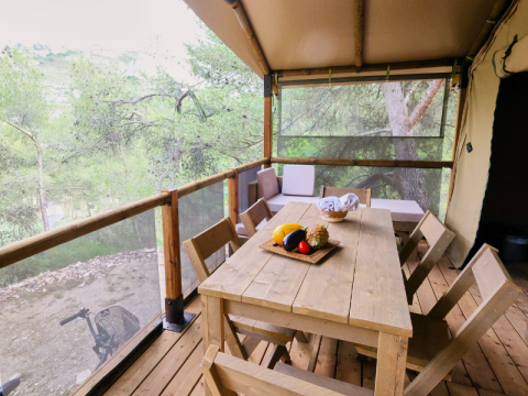 Tavolo e sedie in legno sulla terrazza della tenda safari Premium Lodge al campeggio La Vallée Heureuse, Francia.