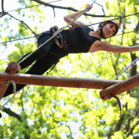 Een vrouw doet een klimparcours in een vakantiepark met glamping, omgeven door groene bomen in de zomer.