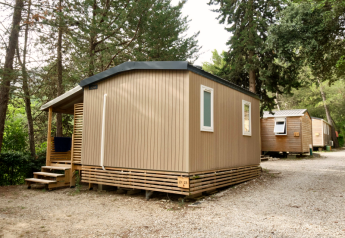 Afbeelding van een moderne Mobile Home Premium, omringd door bomen op een grindrijke camping.