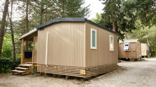 Foto van een moderne Mobile Home Premium, omringd door bomen op een camping met grindbodem.