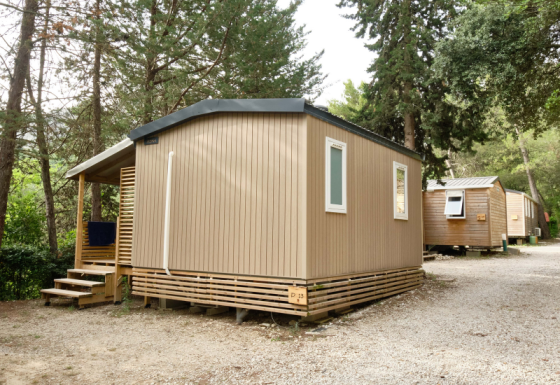 Et billede af en moderne mobilhome Premium, omgivet af træer på en grusbelagt campingplads.