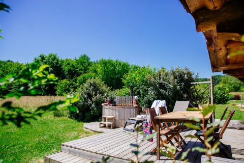 Houten terras met eettafel en houtgestookte hottub bij Log cabin «Trappeur» in Domaine EcÔtelia, Frankrijk.