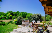 Wooden deck with dining table and hot tub next to lush greenery at Log cabin «Trappeur» in Domaine EcÔtelia, France.