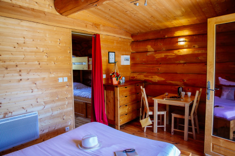 Interno di una baita in legno con letto matrimoniale, letti a castello e tavolo in una casa nella natura.