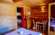 Cozy wooden cabin room with double bed, bunk beds, a table and chairs in a nature house setting.