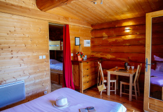 Gemütliches Blockhauszimmer mit Holzdekor, Doppelbett, Etagenbett, Tisch und natürlichem Licht.