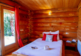 Gemütliches Schlafzimmer aus Holz in einem Naturhaus mit Doppelbett, roten Kissen und Gartenausblick.
