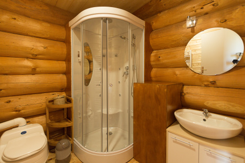 Moderne badkamer in een houten chalet met douche, lavabo, toilet en ronde spiegel tegen de wand.