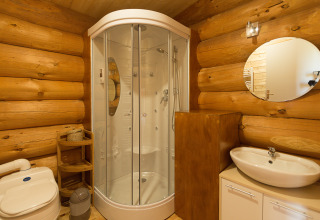 Salle de bain moderne dans une cabane en bois avec douche, lavabo, toilettes et miroir rond au mur.