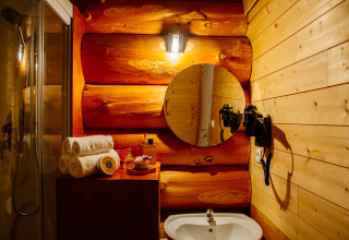 Gemütliches Badezimmer in einem Naturhaus mit Holzwänden, rundem Spiegel, Waschbecken und Handtüchern.