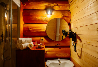 Gemütliches Badezimmer in einem Naturhaus mit Holzwänden, rundem Spiegel, Waschbecken und Handtüchern.