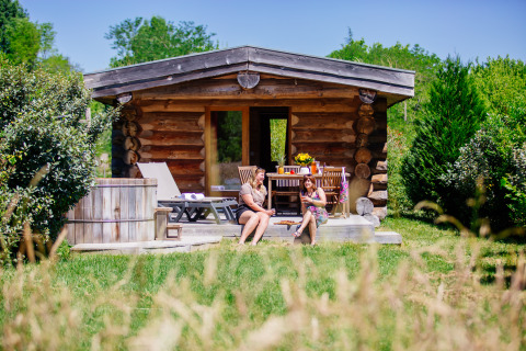 Twee vrouwen ontspannen samen voor een houten blokhut met hottub bij Domaine EcÔtelia in Frankrijk.