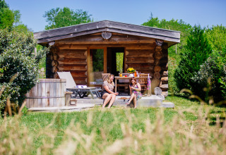 Due donne si rilassano davanti a una baita in legno con vasca esterna immersa nel verde a Domaine EcÔtelia, Francia.