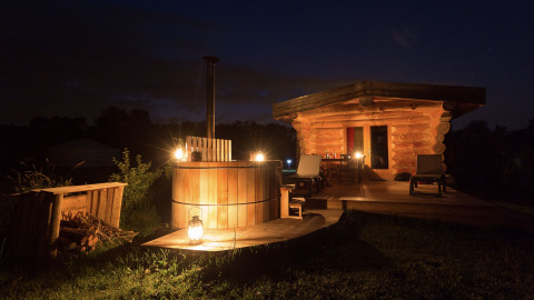 Gezellig verlichte blokhut en houten hottub ’s nachts bij Domaine EcÔtelia in Frankrijk.