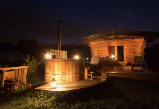 Cabaña de troncos iluminada y bañera de madera al aire libre en Domaine EcÔtelia, Francia, por la noche.