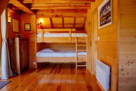 Træhusværelse i Log cabin Temple perché på Domaine EcÔtelia, Frankrig, med køjesenge og træinteriør.