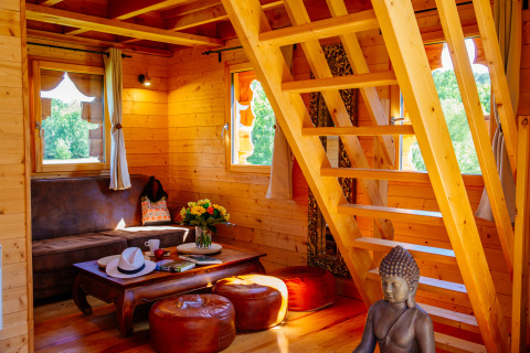 Boomhutinterieur met houten trap, zithoek, Boeddhabeeld en veel licht bij Domaine EcÔtelia in Frankrijk.