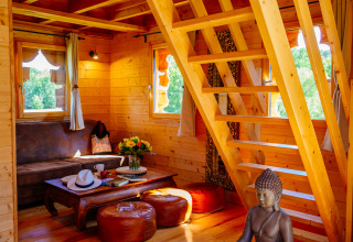 Cozy tree house interior at Domaine EcÔtelia, with wooden stairs, lounge area, Buddha statue and sunlight.