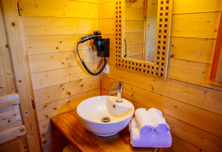 Salle de bain en cabane avec vasque ronde, miroir, sèche-cheveux mural et serviettes roulées sur plan en bois.
